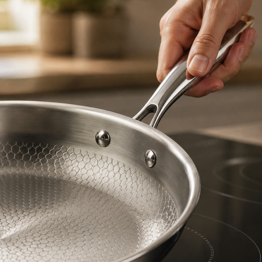 A hand gripping the stainless handle of The Sunday Pan on an induction hob