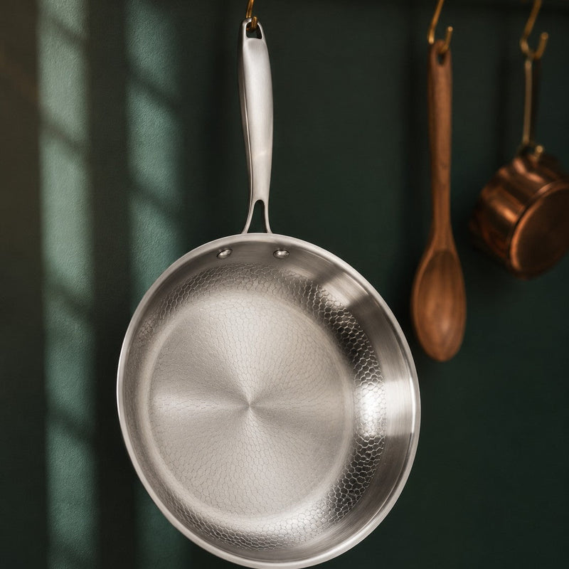 The Sunday Pan hanging from a brass kitchen rail against a deep green wall