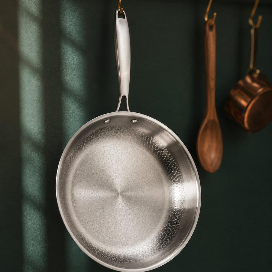 The Sunday Pan hanging from a brass kitchen rail against a deep green wall