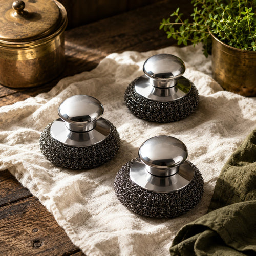 Three chainmail scrubbers with polished steel knobs on cream linen